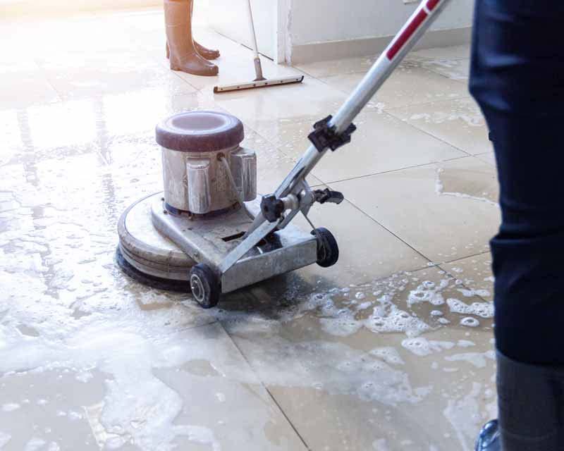 Cleaning professional using a floor machine for specialized janitorial floor care in a commercial building