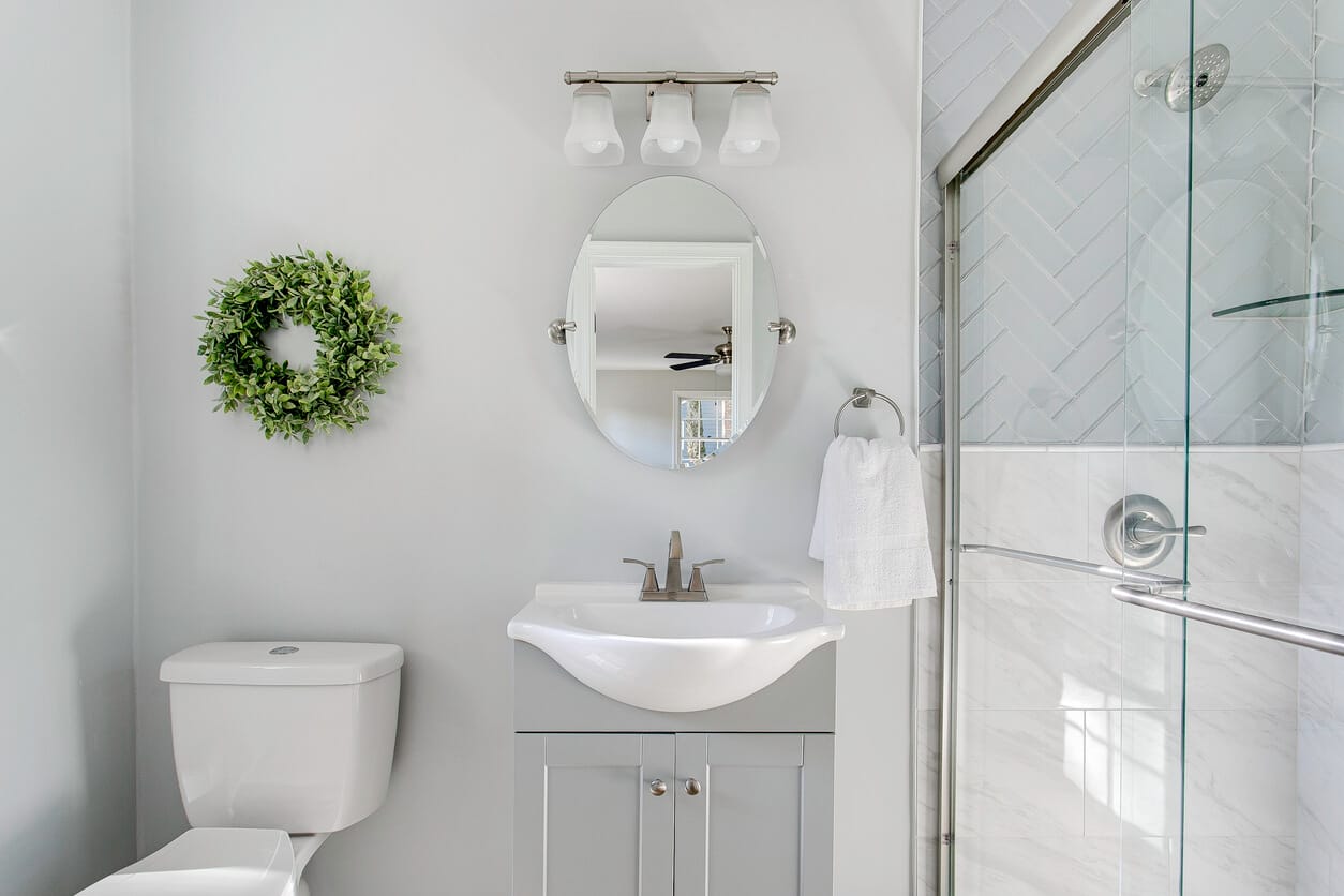 Clean gray guest bathroom with a small green wreath, oval mirror and fresh hand towel