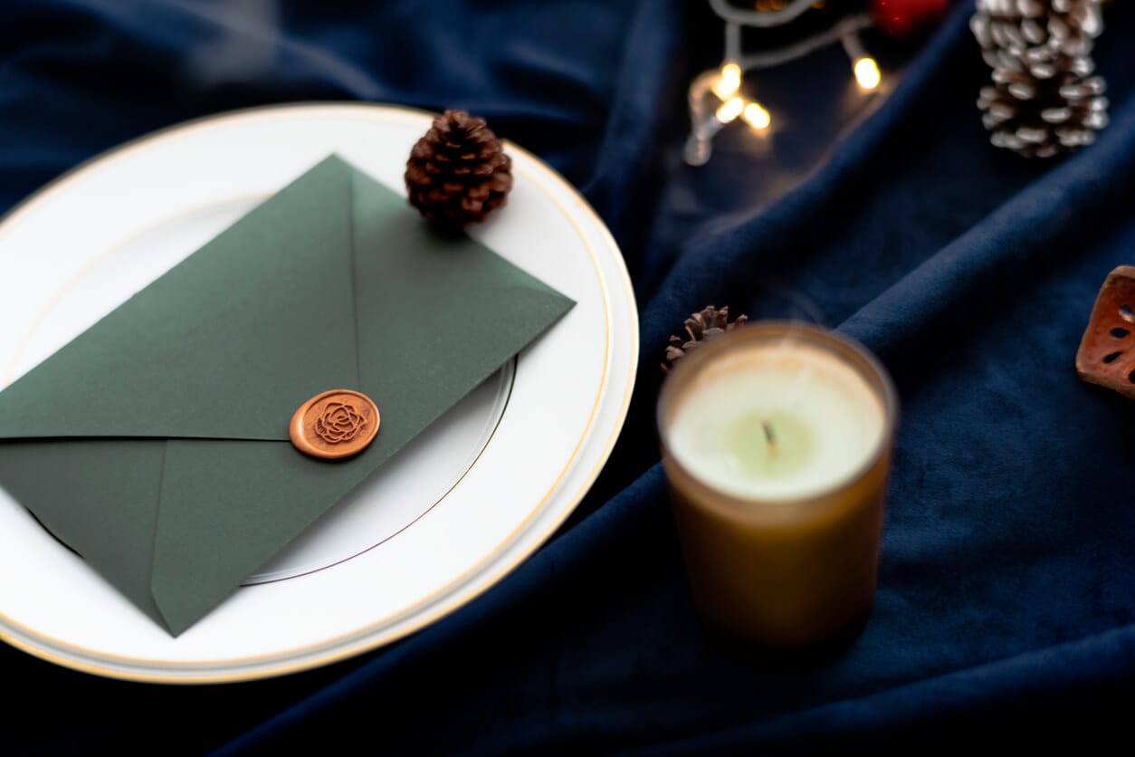 Green envelope with a wax seal on a gold-rimmed plate beside a candle and string lights