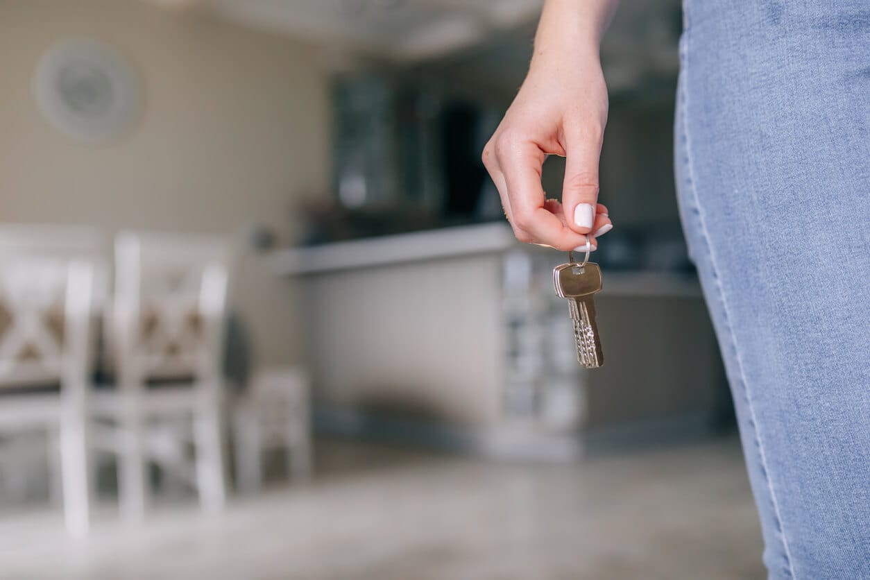 Hand holding a set of keys in an empty rental with a kitchen behind