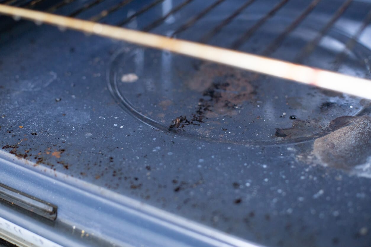 Dirty oven interior with burnt food residue on the floor of the oven below the racks