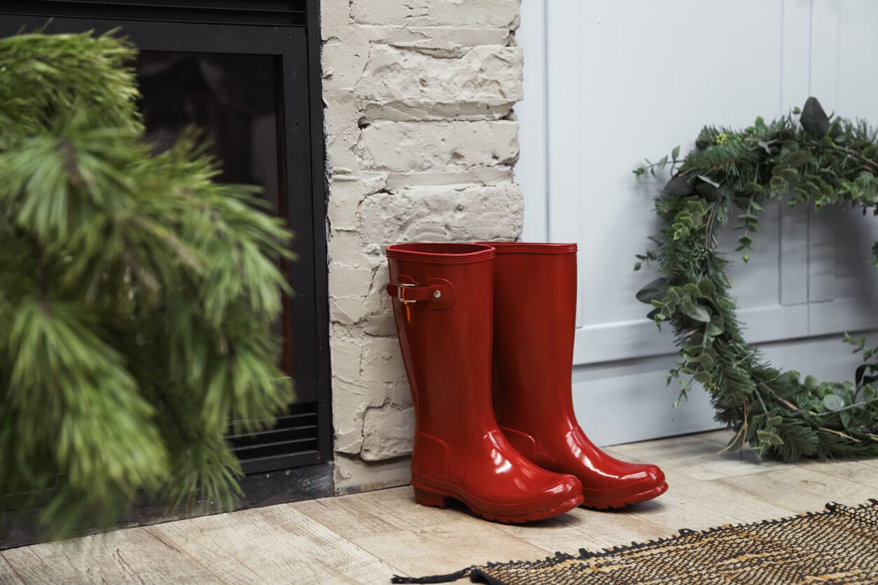 Red rain boots by a fireplace next to a holiday wreath and pine branches
